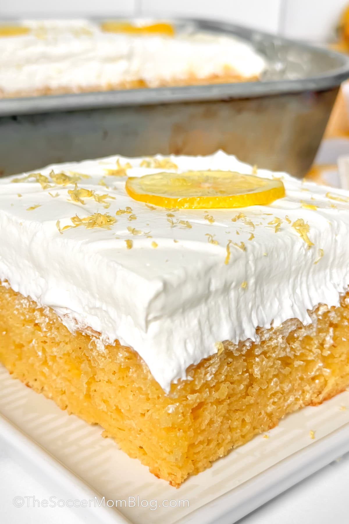 close up of a slice of lemon sheet cake topped with whipped cream.