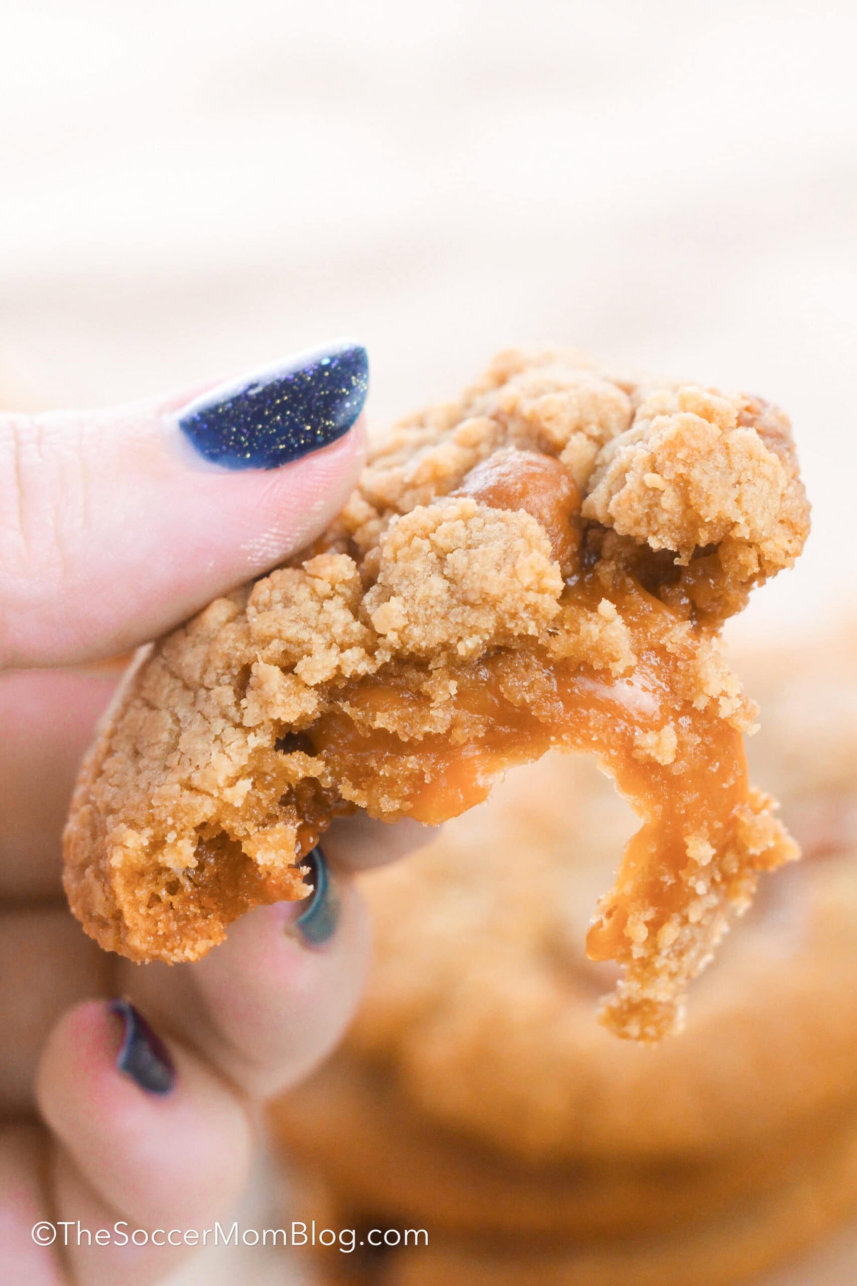 holding half of a caramel filled cookie with melted caramel oozing out.