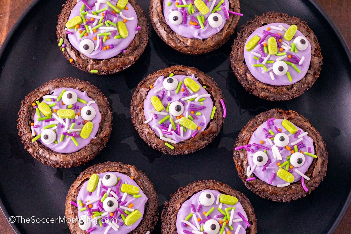 a plate of bite-sized witches cauldron brownies filled with frosting and sprinkles.