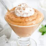 Pumpkin Pudding in a glass serving dish with whipped cream and a dusting of cinnamon.